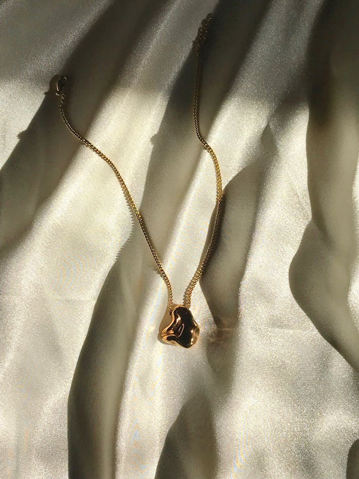 Close-up of an elegant gold necklace on soft satin cloth, capturing light reflections.